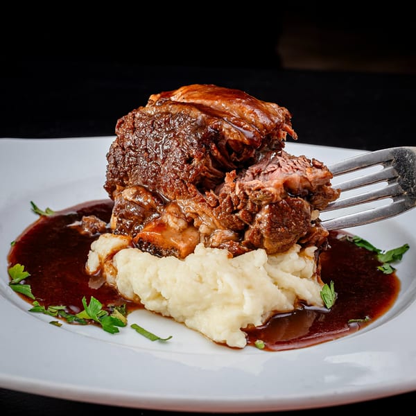 Braised short rib with mashed potatoes and gravy, with a fork lifting a piece of meat.
