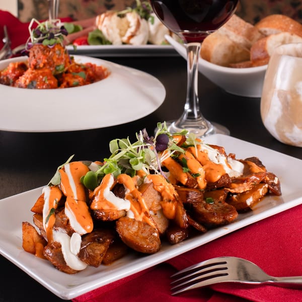 Crispy potatoes with white and orange sauces, microgreens, and meatballs in the background.