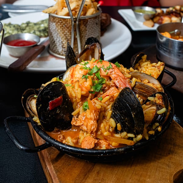 Close-up of a seafood paella with mussels, shrimp, and rice in a black pan on a wooden board.