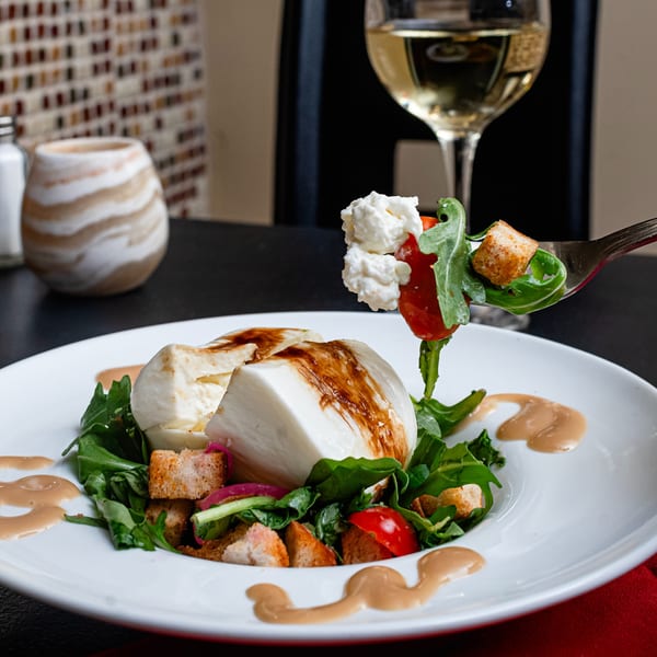 Burrata cheese salad with arugula, tomatoes, croutons, balsamic glaze, and a forkful of ingredients.